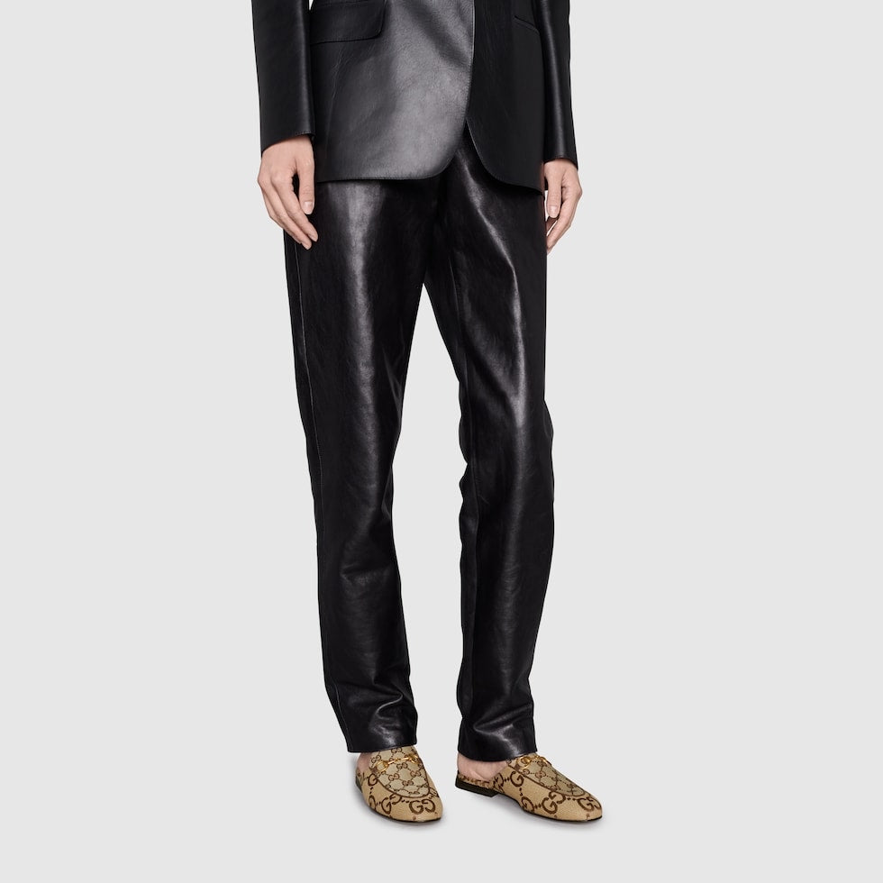 Person wearing a black leather suit with patterned shoes on a light gray background