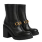 Black ankle boots with gold Gucci logo on a light gray background