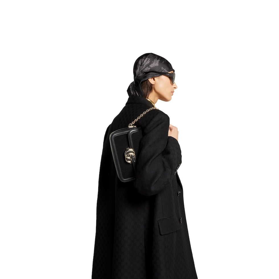 Person wearing a black coat and headscarf with a black handbag on a white background