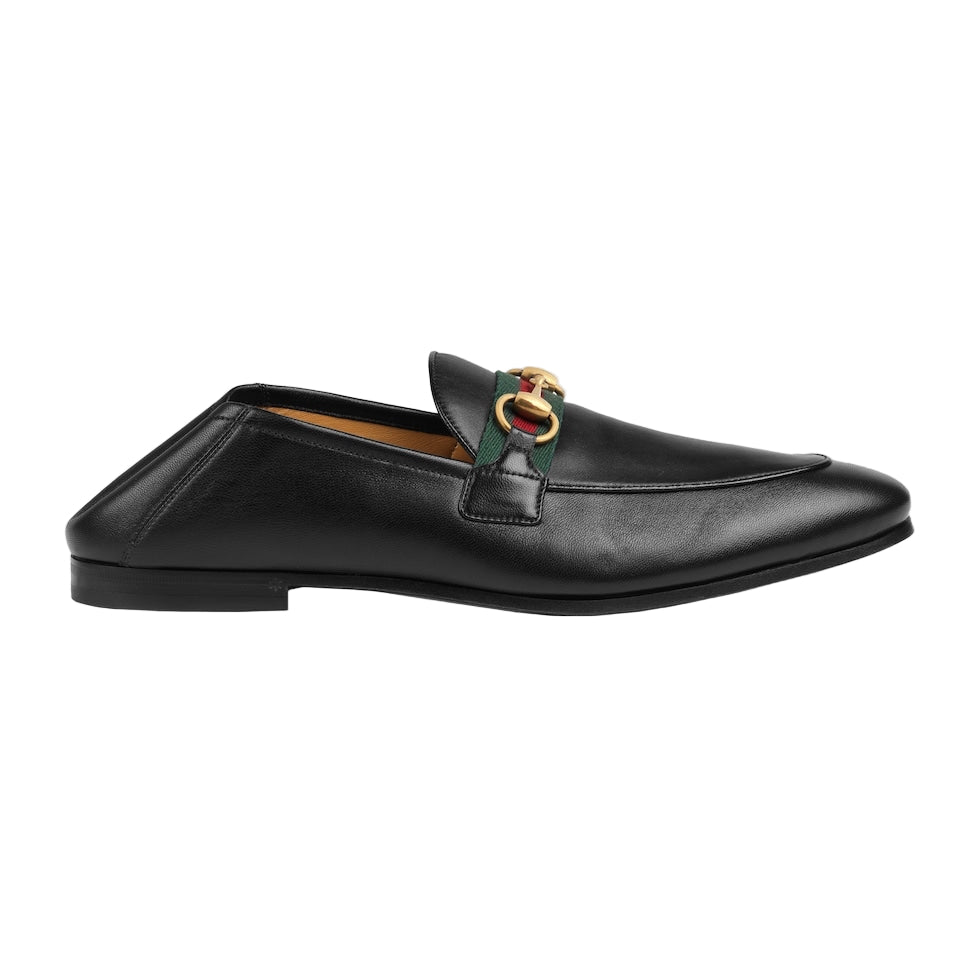 Black leather loafer with a gold and green horsebit on a light gray background