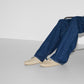 Person wearing blue jeans and beige shoes sitting on a white surface with a white background