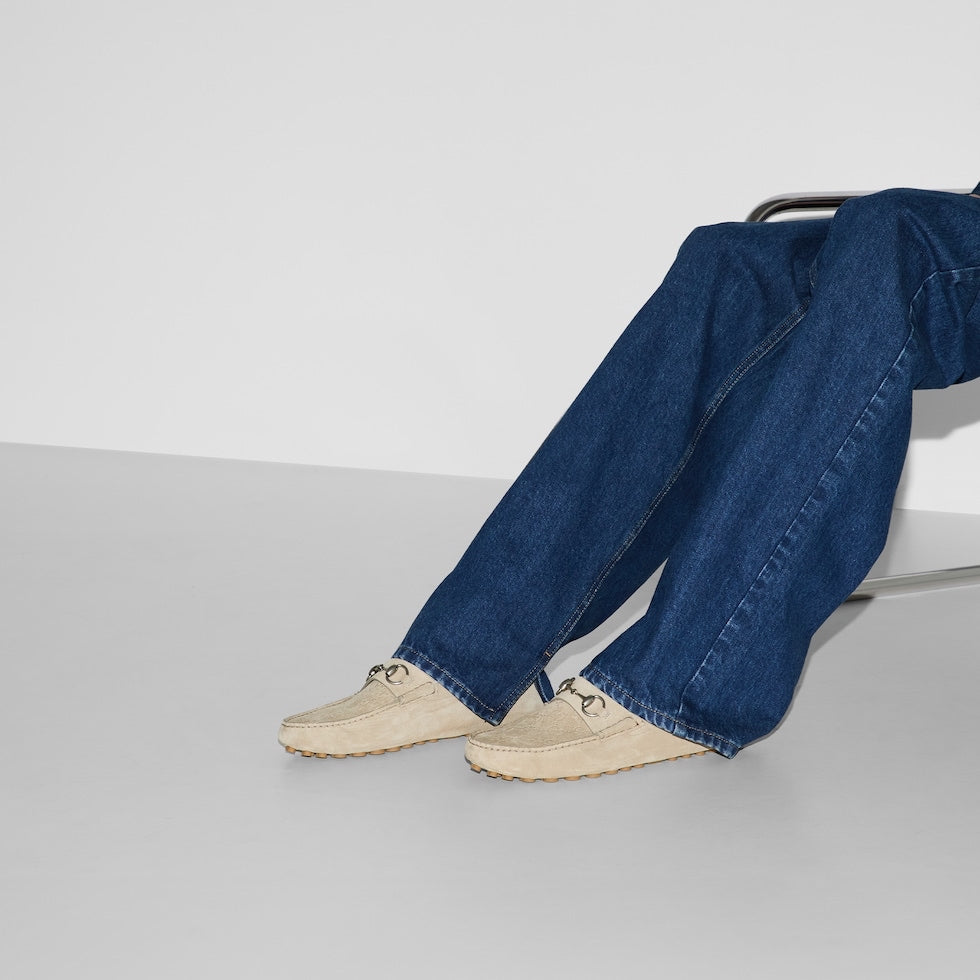 Person wearing blue jeans and beige shoes sitting on a white surface with a white background