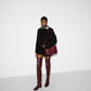 Person wearing a black outfit with burgundy knee-high boots and a matching bag on a white background