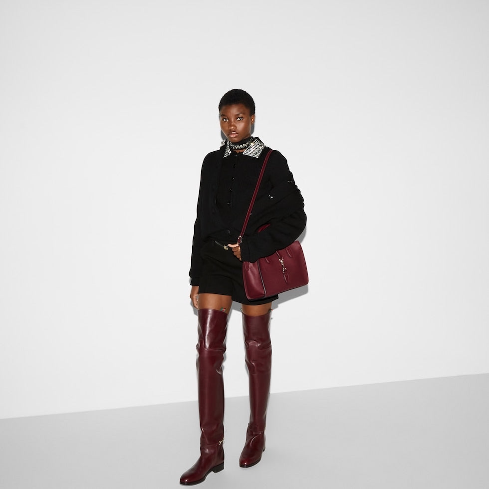 Person wearing a black outfit with burgundy knee-high boots and a matching bag on a white background