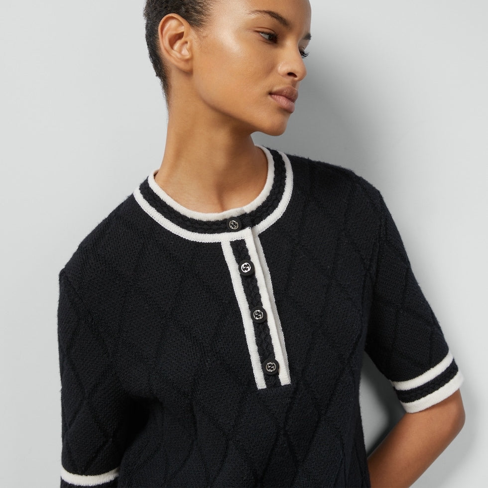 Woman wearing a blackGucci  dress with white trim on a plain background