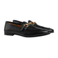 Black loafers with a decorative band on a light gray background