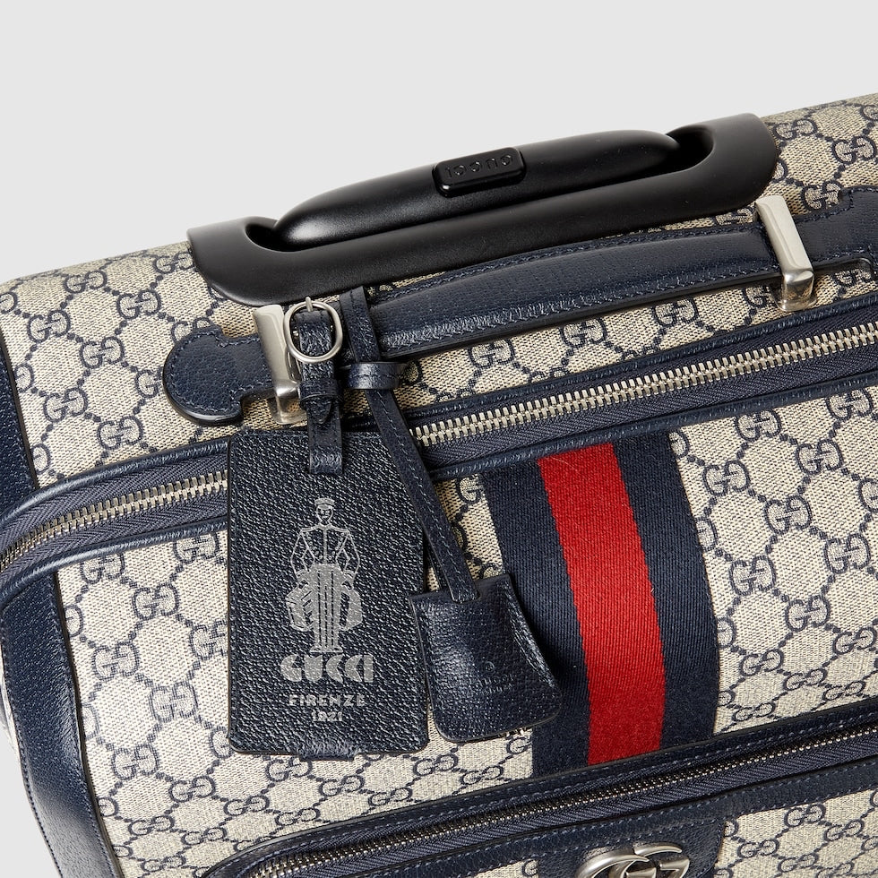 Designer luggage with visible Gucci logo and tag on a light gray background