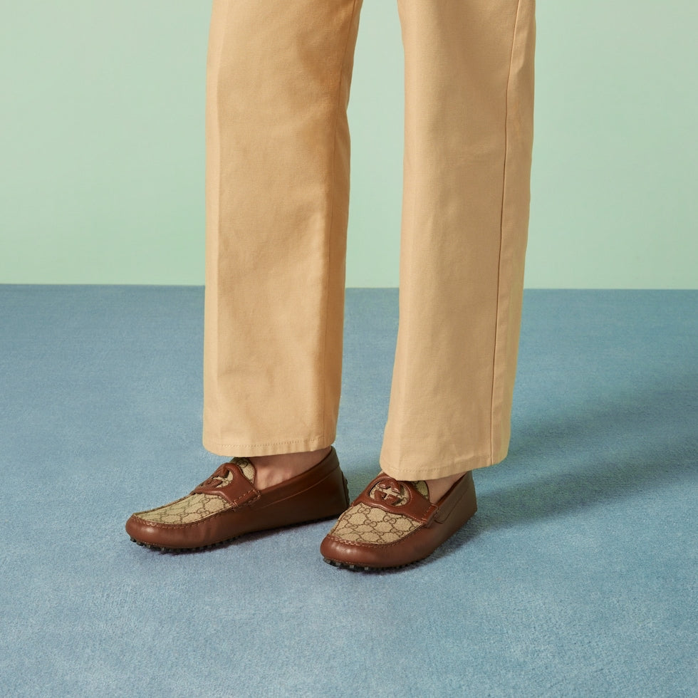 Brown loafers with Gucci logo worn with beige pants on a blue and green background