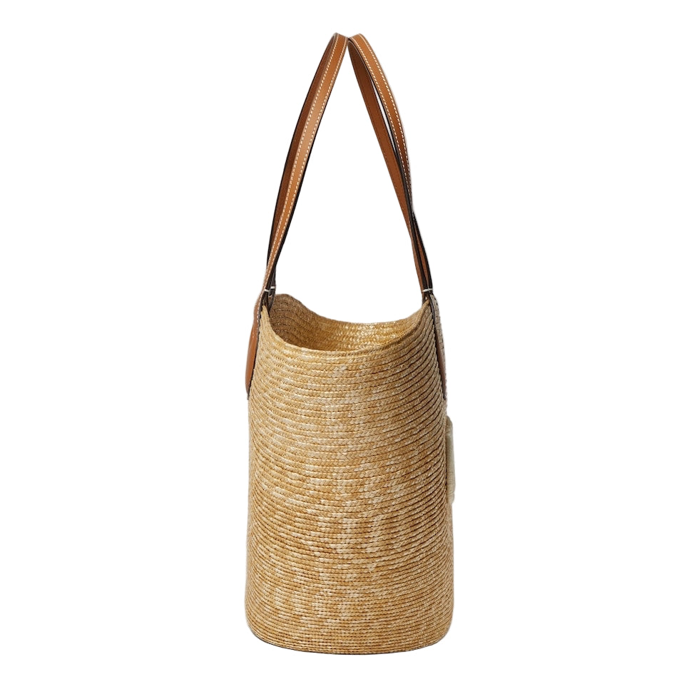 Woven straw bag with brown leather handle on a light gray background