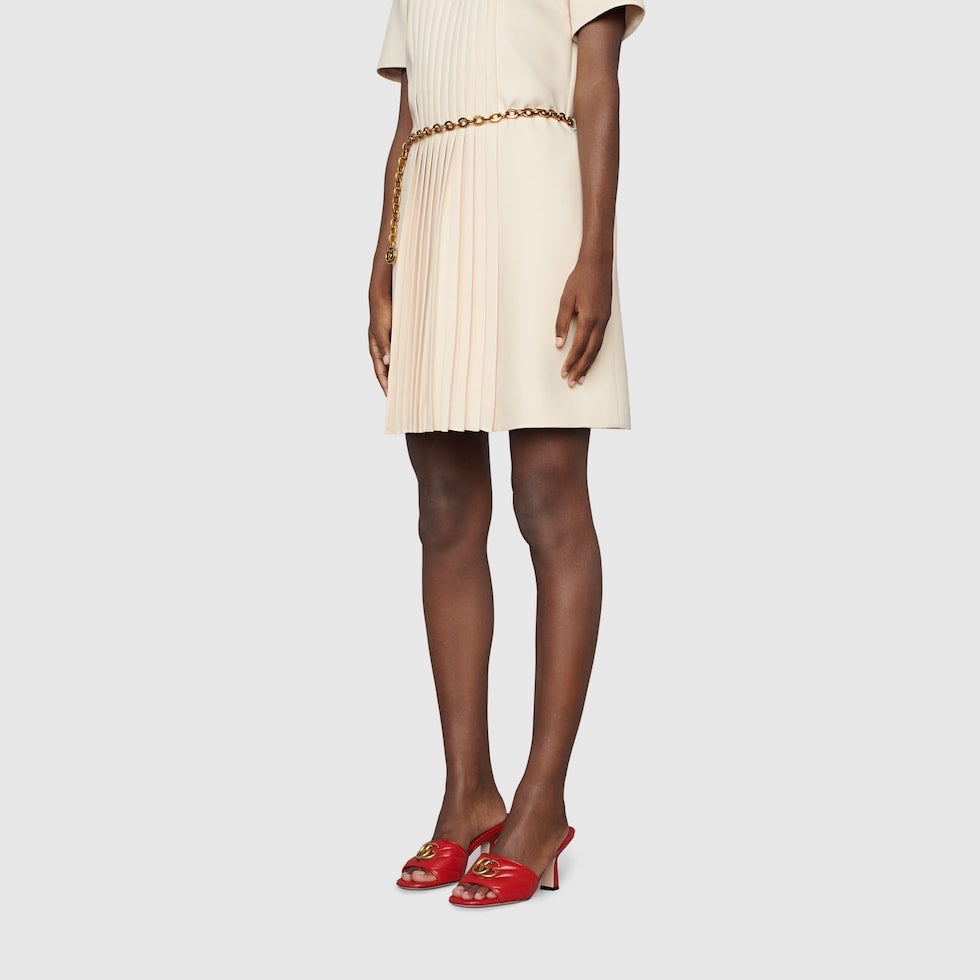 Person wearing a beige dress with a gold belt and red shoes on a light gray background