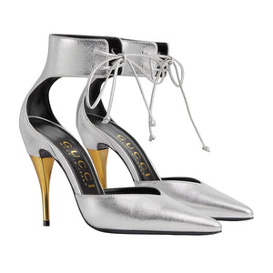 Silver high-heeled shoes with gold accents on a light gray background