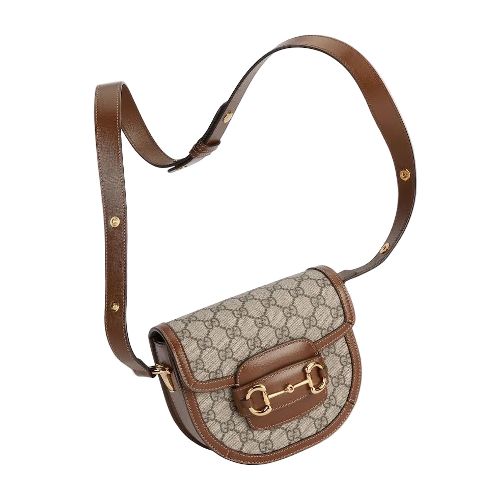 Designer handbag with brown leather strap and gold hardware on a light gray background