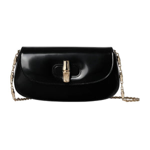 Black handbag with gold clasp and chain strap on a light gray background
