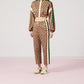 Person wearing a Gucci tracksuit with a brown pattern and red, white, and green stripes on a light pink background.