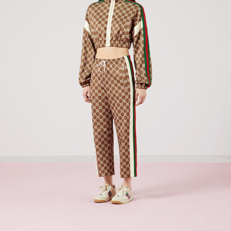 Person wearing a Gucci tracksuit with a brown pattern and red, white, and green stripes on a light pink background.