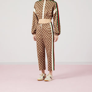 Person wearing a Gucci tracksuit with a brown pattern and red, white, and green stripes on a light pink background.