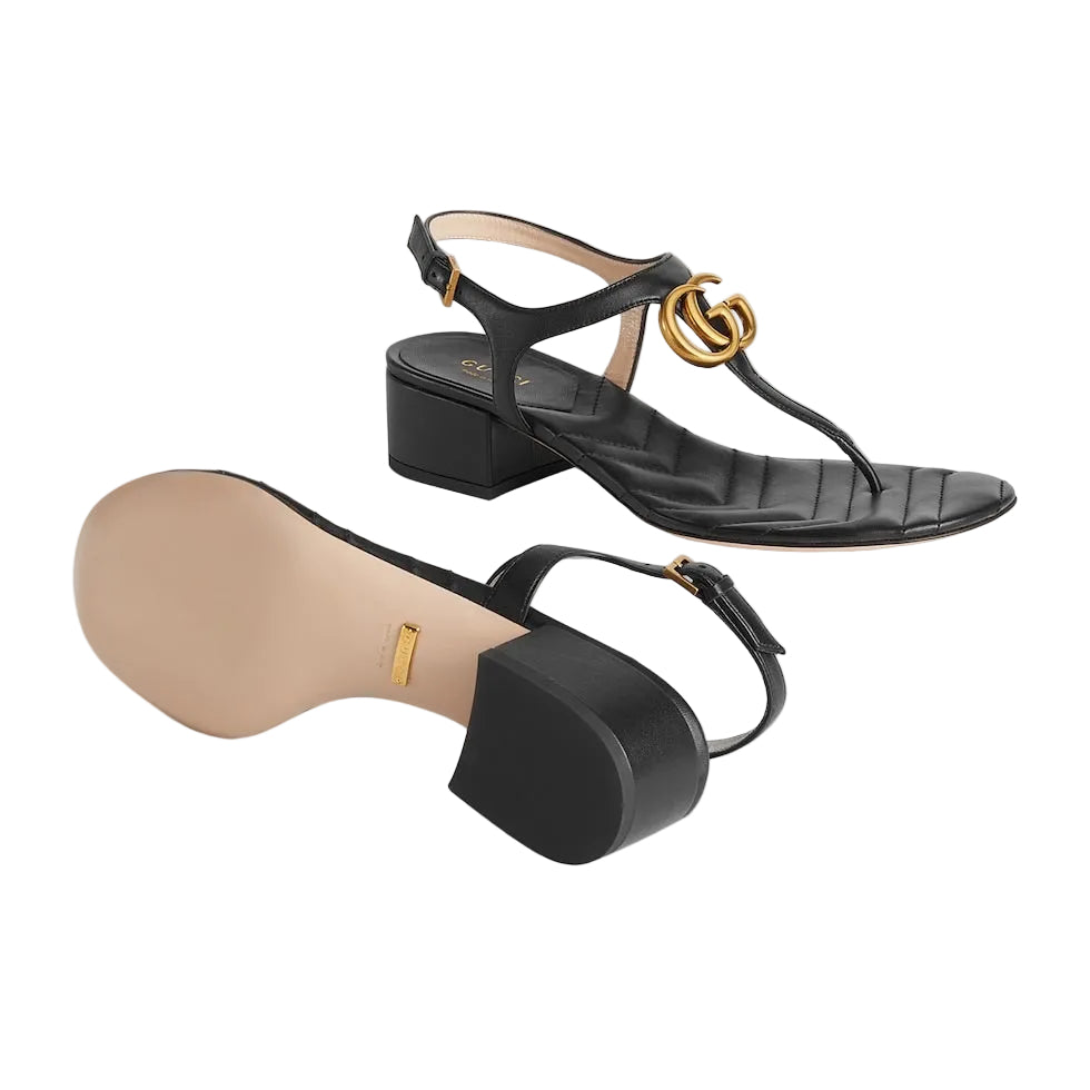 Black high-heeled sandals with gold accents on a light gray background