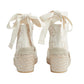Pair of white lace-up shoes with raffia sole on a light gray background