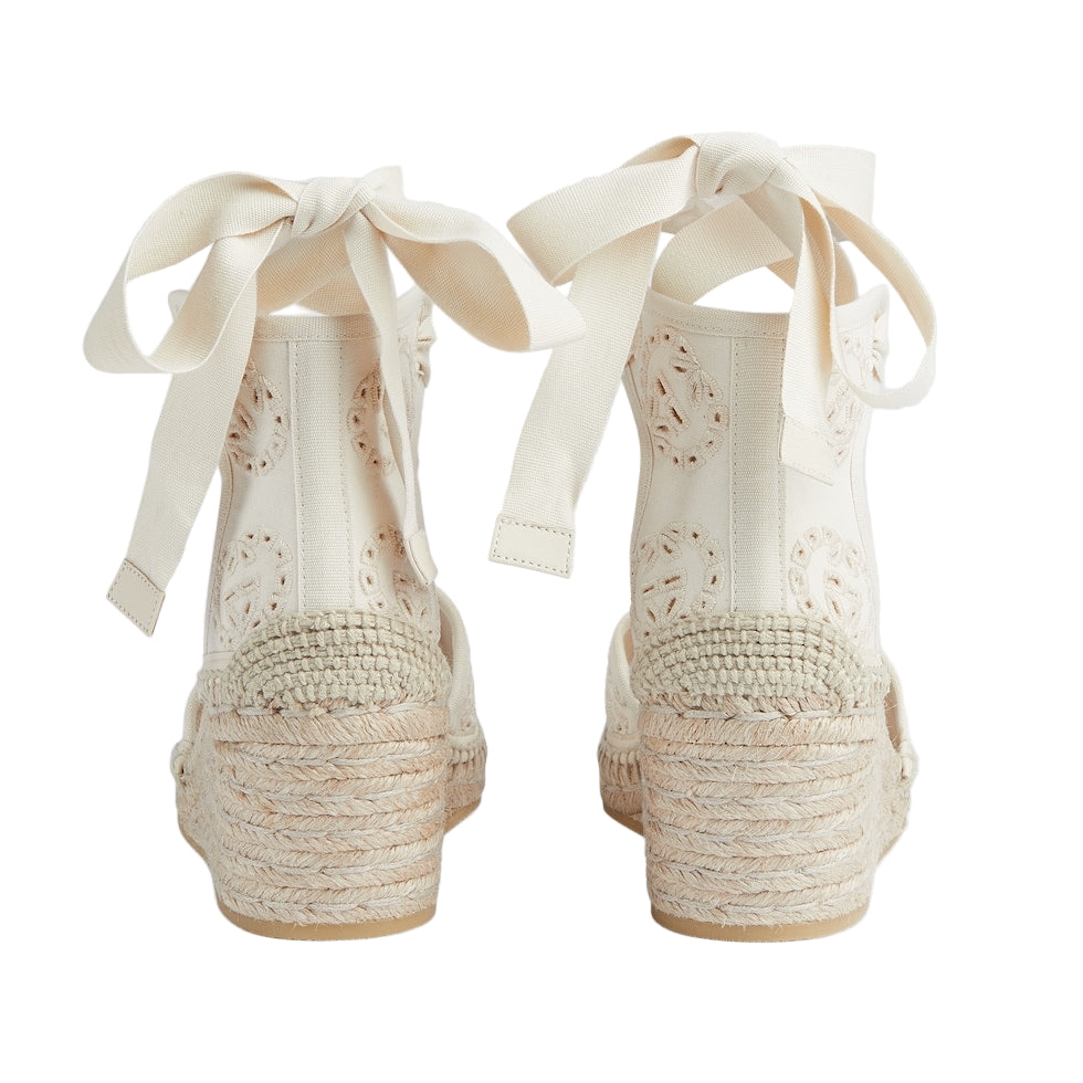 Pair of white lace-up shoes with raffia sole on a light gray background