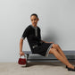 Woman in a black gucci dress with white trim sitting on a bench holding a red handbag.