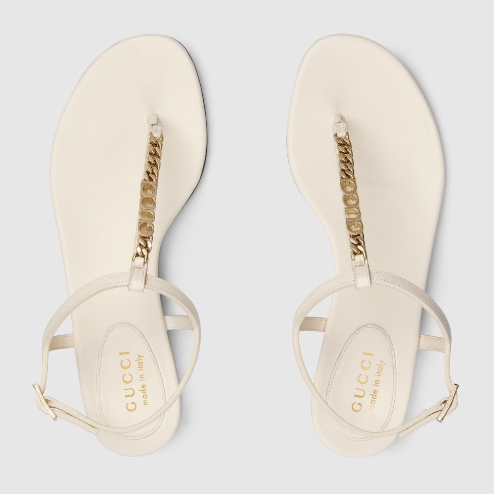 Pair of Gucci sandals with gold chain detail on a light gray background