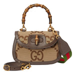 Designer handbag with bamboo handle and visible brand logo on a light gray background