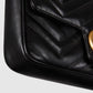 Close-up of a black quilted handbag with a gold clasp on a light gray background