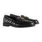 Black loafers with gold buckles on a light gray background