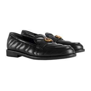 Black loafers with gold buckles on a light gray background