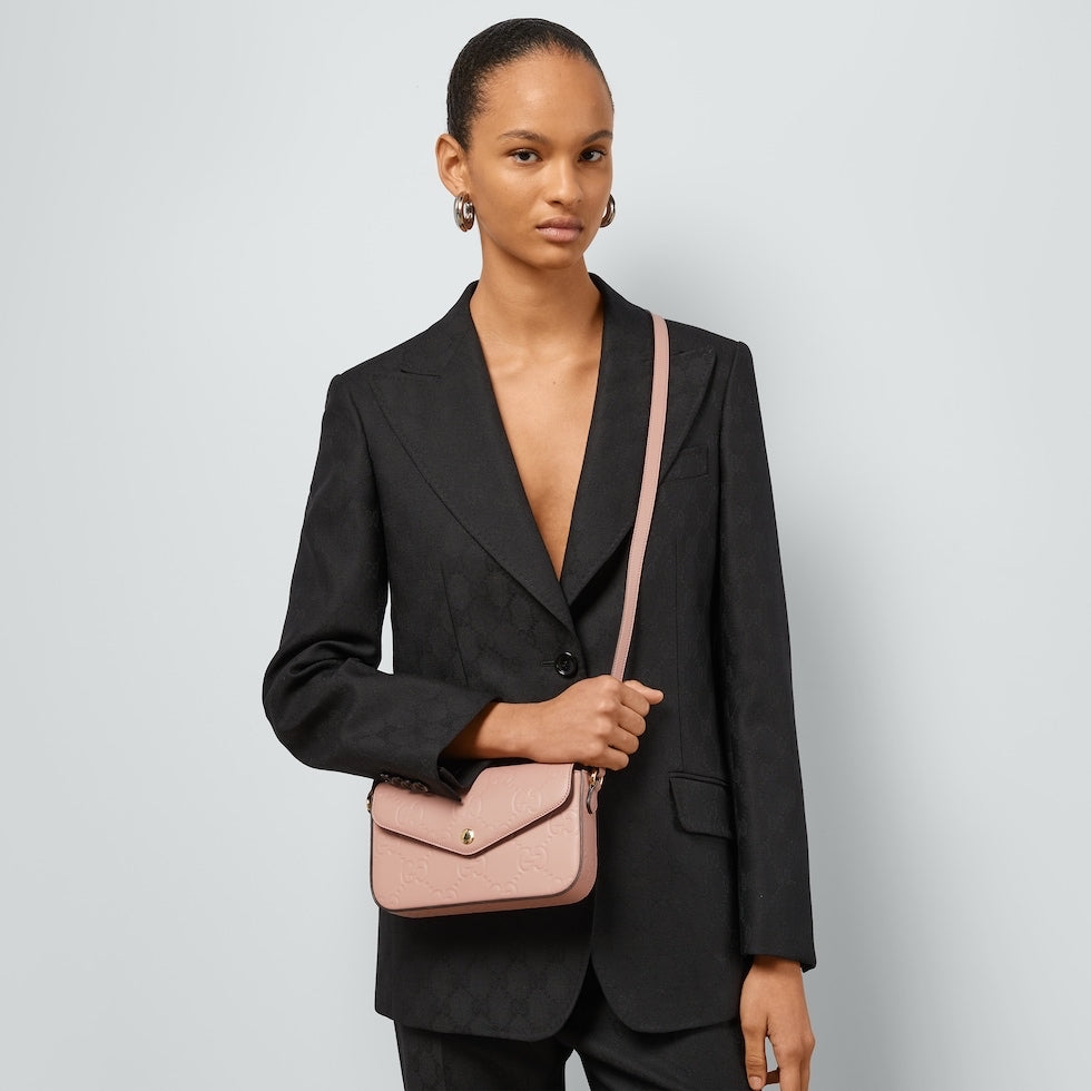 Woman wearing a black suit with a pink handbag on a light gray background