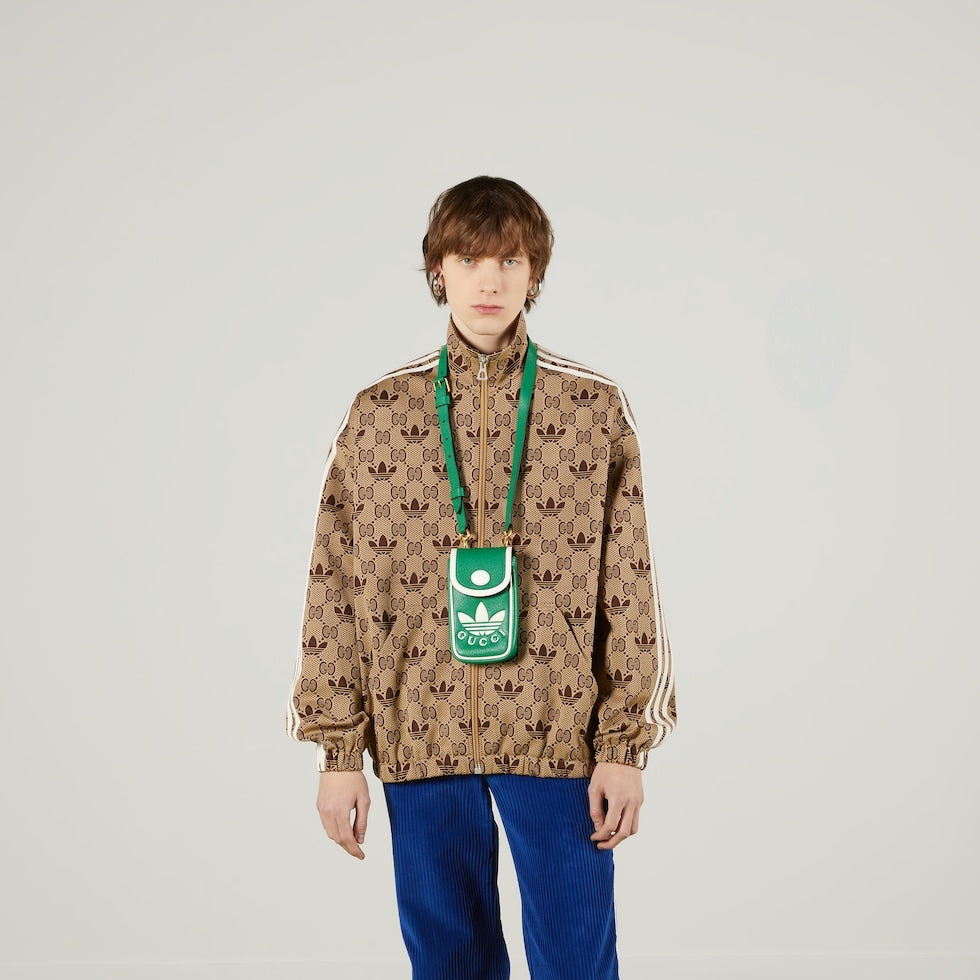 Person wearing a patterned jacket with a green Adidas bag over their shoulder on a plain background