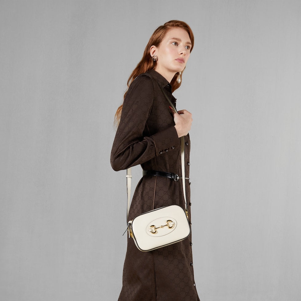 Woman holding a white handbag with a gold clasp against a gray background