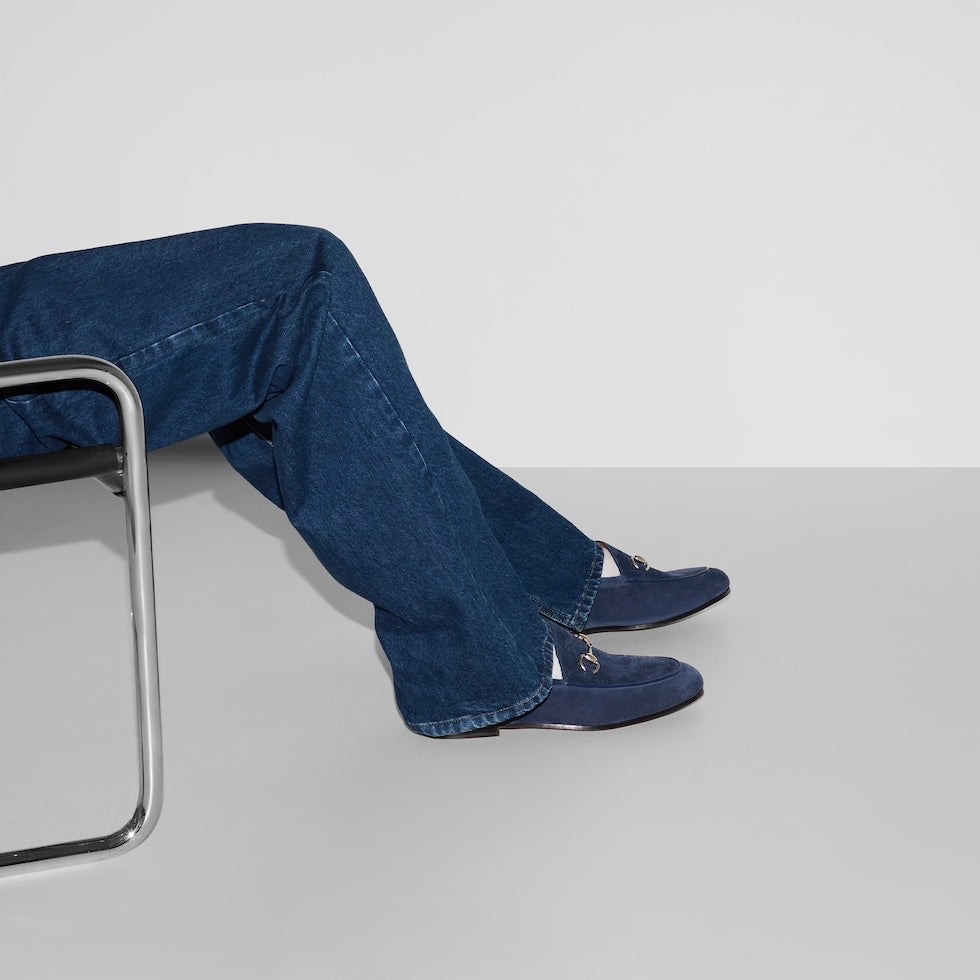 Person wearing blue jeans and shoes sitting on a chair with a plain background