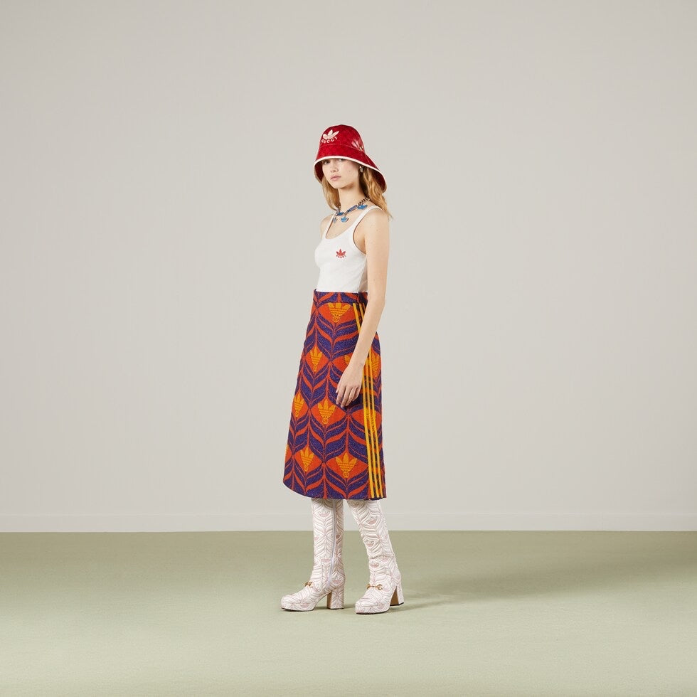Woman wearing a patterned skirt, white top, and red hat against a plain background