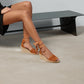 Brown wedge sandals worn by a person sitting on a black bench.