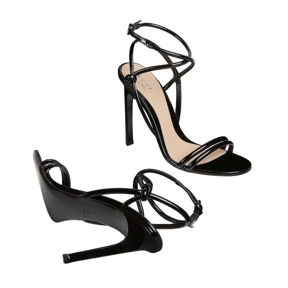 Black high-heeled sandals with strappy design on a light gray background