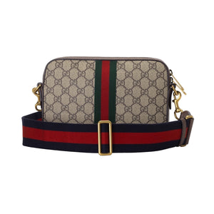 Designer handbag with patterned surface and colorful strap on a light gray background