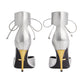 Pair of silver high-heeled shoes with yellow soles on a light gray background