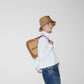 Person wearing a white shirt, blue jeans, and a brown bucket hat, holding a brown leather bag with a pattern.