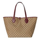 Beige handbag with brown pattern and red handles on a light gray background