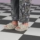Person wearing beige platform sandals and embellished jeans on a checkered floor.