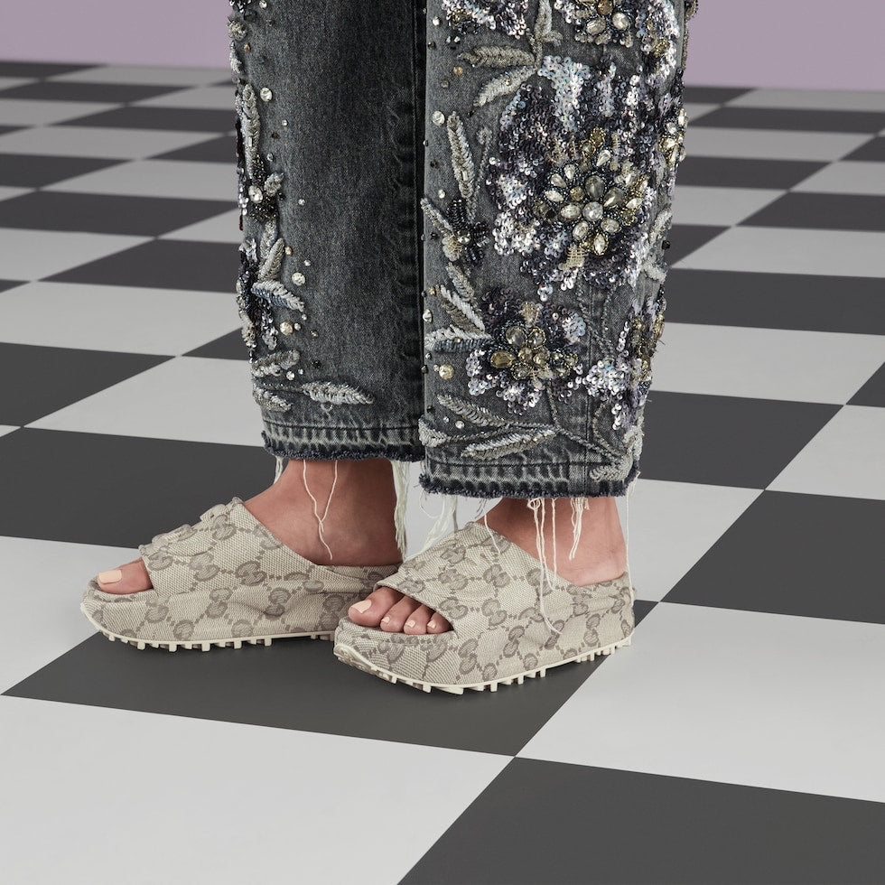 Person wearing beige platform sandals and embellished jeans on a checkered floor.