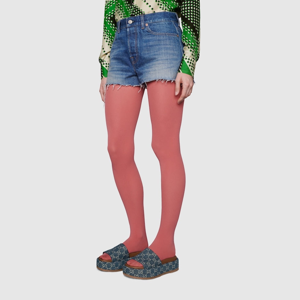 Person wearing denim shorts and pink tights on a plain background