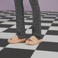 Person wearing beige sandals with a pattern on a checkered floor.