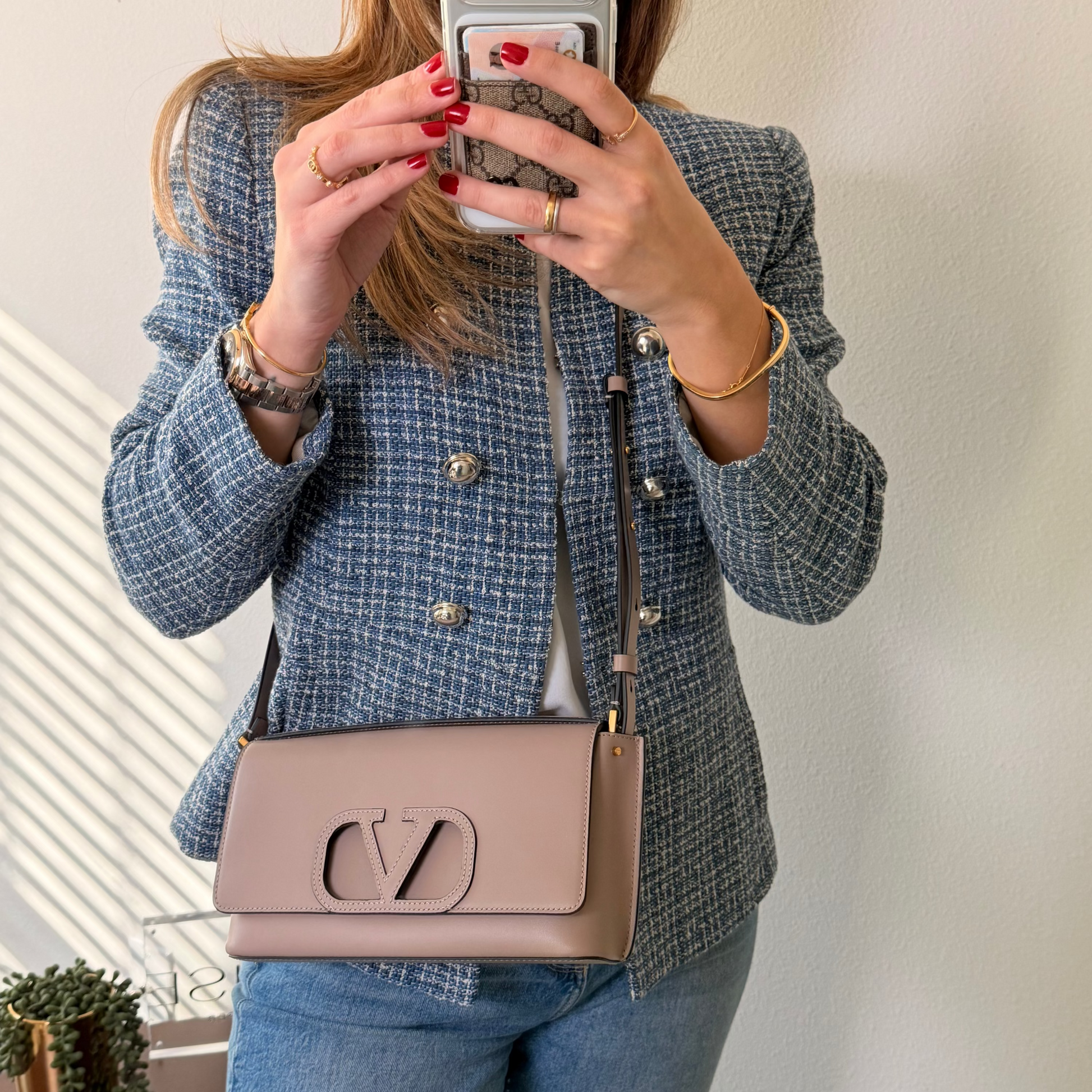 Woman taking a mirror selfie wearing a blue tweed jacket and holding a beige handbag with a logo.