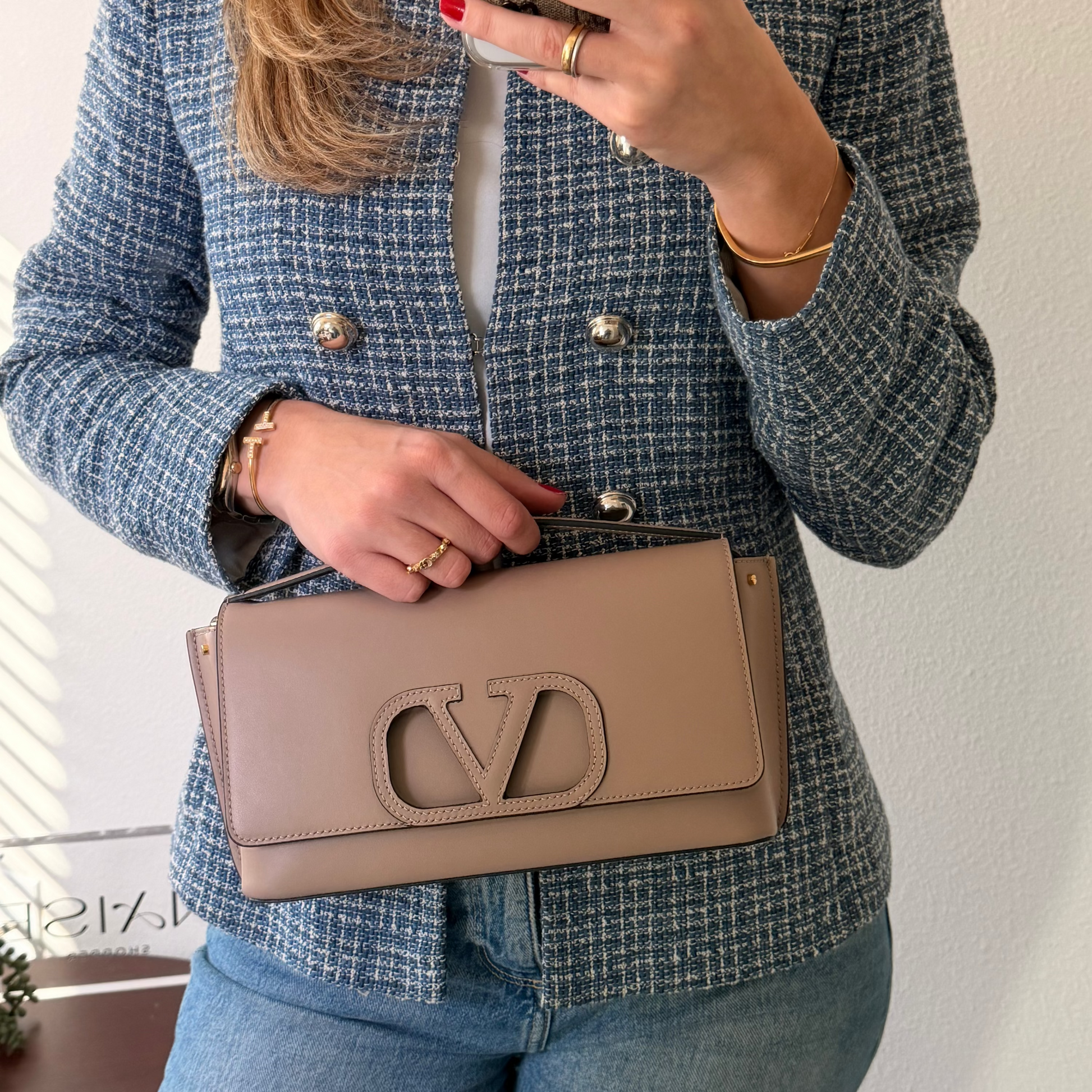 Person wearing a blue textured jacket holding a beige handbag with a logo.