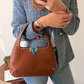 Person holding a brown leather handbag with a blue checkered jacket and jeans.