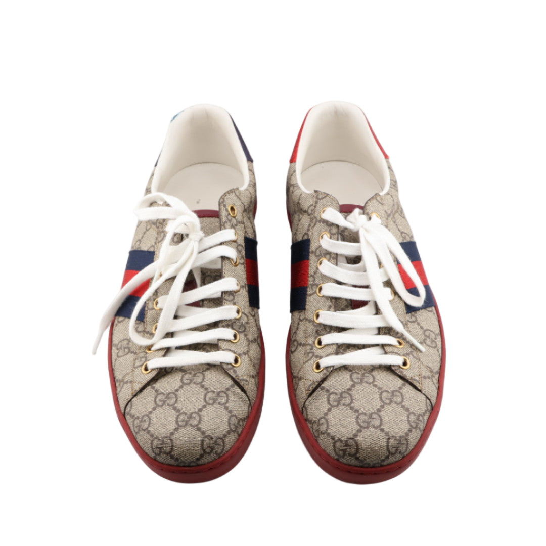 Pair of Gucci sneakers with distinctive pattern and red soles on a white background