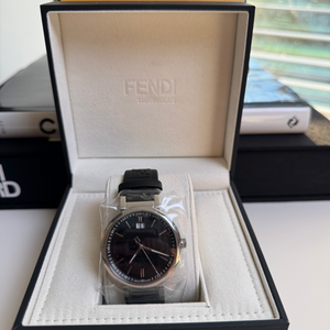 Fendi branded watch presented in an open white and black box, with a brown leather band and a silver-colored dial.