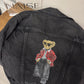 Black denim jacket with a bear graphic on a wooden surface